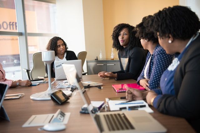 Group of peple having a meeting at a conference table filled with laptops and notepads